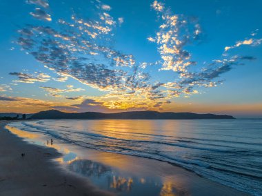 Sonbahar gündoğumu gökyüzünde güzel bulutlar ve nemli kumdaki yansımalarla Orta Sahildeki Umina Sahili, NSW, Avustralya.
