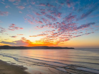 Sonbahar gündoğumu gökyüzünde güzel bulutlar ve nemli kumdaki yansımalarla Orta Sahildeki Umina Sahili, NSW, Avustralya.