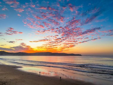Sonbahar gündoğumu gökyüzünde güzel bulutlar ve nemli kumdaki yansımalarla Orta Sahildeki Umina Sahili, NSW, Avustralya.