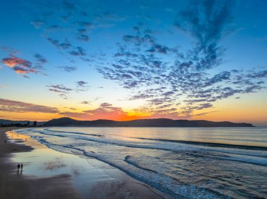 Sonbahar gündoğumu gökyüzünde güzel bulutlar ve nemli kumdaki yansımalarla Orta Sahildeki Umina Sahili, NSW, Avustralya.