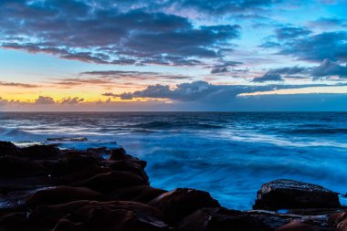 Central Coast, NSW, Avustralya 'daki Kuzey Avoca Kaya Platformu' nda bulutlu ve dalgalı gün doğumu deniz manzarası.