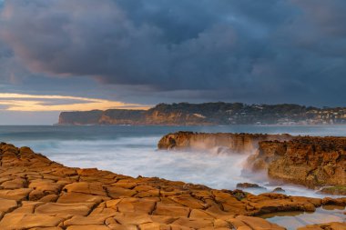 Central Coast, NSW, Avustralya 'daki Kuzey Avoca Kaya Platformu' nda bulutlu ve dalgalı gün doğumu deniz manzarası.