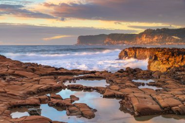 Central Coast, NSW, Avustralya 'daki Kuzey Avoca Kaya Platformu' nda bulutlu ve dalgalı gün doğumu deniz manzarası.
