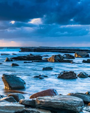 Terrigal, NSW, Avustralya 'daki The Skillion' da sonbahar gündoğumu bulutları ve kayalarla birlikte deniz manzarası.