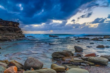 Terrigal, NSW, Avustralya 'daki The Skillion' da sonbahar gündoğumu bulutları ve kayalarla birlikte deniz manzarası.