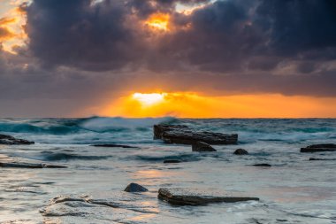 Güneşin ışınlarıyla sonbahar gündoğumu denizin üzerinde bulutlar arasında ışıldıyor ve Terrigal, NSW, Avustralya 'daki Skillion' da kayalar var..