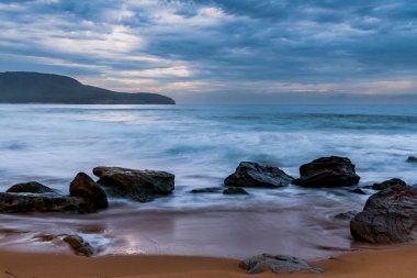 Central Coast, NSW, Avustralya 'daki Killcare Sahili' nde dalgalar ve kayalarla bulutlu bir deniz doğumu..