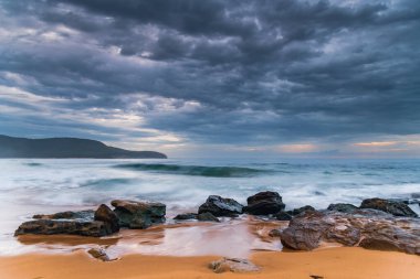 Central Coast, NSW, Avustralya 'daki Killcare Sahili' nde dalgalar ve kayalarla bulutlu bir deniz doğumu..