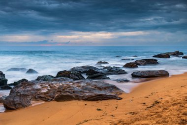 Central Coast, NSW, Avustralya 'daki Killcare Sahili' nde dalgalar ve kayalarla bulutlu bir deniz doğumu..