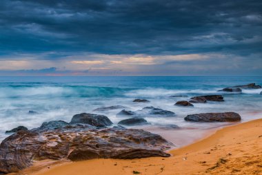 Central Coast, NSW, Avustralya 'daki Killcare Sahili' nde dalgalar ve kayalarla bulutlu bir deniz doğumu..