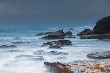 Central Coast, NSW, Avustralya 'daki Killcare Sahili' nde dalgalar ve kayalarla bulutlu bir deniz doğumu..
