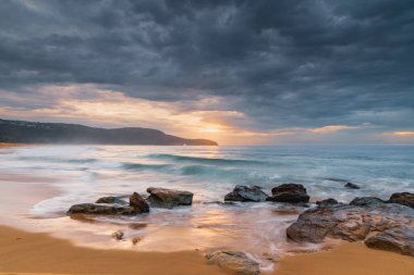 Central Coast, NSW, Avustralya 'daki Killcare Sahili' nde dalgalar ve kayalarla bulutlu bir deniz doğumu..