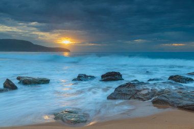 Central Coast, NSW, Avustralya 'daki Killcare Sahili' nde dalgalar ve kayalarla bulutlu bir deniz doğumu..