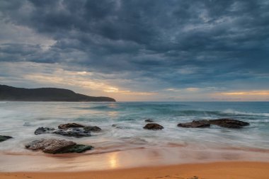 Central Coast, NSW, Avustralya 'daki Killcare Sahili' nde dalgalar ve kayalarla bulutlu bir deniz doğumu..