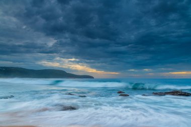 Central Coast, NSW, Avustralya 'daki Killcare Sahili' nde dalgalar ve kayalarla bulutlu bir deniz doğumu..