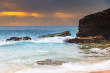 Central Coast, NSW, Avustralya 'daki Killcare Sahili' nde dalgalar ve kayalarla bulutlu bir deniz doğumu..