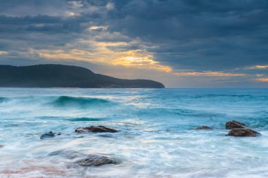 Central Coast, NSW, Avustralya 'daki Killcare Sahili' nde dalgalar ve kayalarla bulutlu bir deniz doğumu..