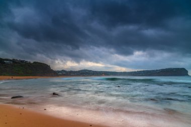 Gökyüzü yağmur bulutu ile dolu hava gündoğumu deniz manzarası ve Orta Sahildeki Macmaster Sahili 'nde küçük dalgalar, NSW, Avustralya.