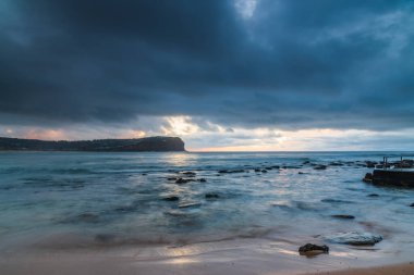 Gökyüzü yağmur bulutu ile dolu hava gündoğumu deniz manzarası ve Orta Sahildeki Macmaster Sahili 'nde küçük dalgalar, NSW, Avustralya.