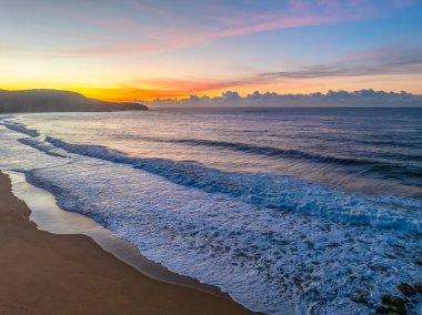 Gündoğumu denizi yumuşak bulutlu ve dalgalı Orta Sahildeki Killcare Sahili, NSW, Avustralya.