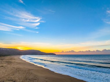 Gündoğumu denizi yumuşak bulutlu ve dalgalı Orta Sahildeki Killcare Sahili, NSW, Avustralya.