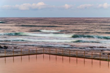 Towradgi Sahili 'nde gün batımında Woolongong, NSW, Avustralya' da siyah kayalar var. Towradgi, 