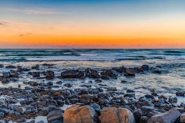 Towradgi Sahili 'nde gün batımında Woolongong, NSW, Avustralya' da siyah kayalar var. Towradgi, 