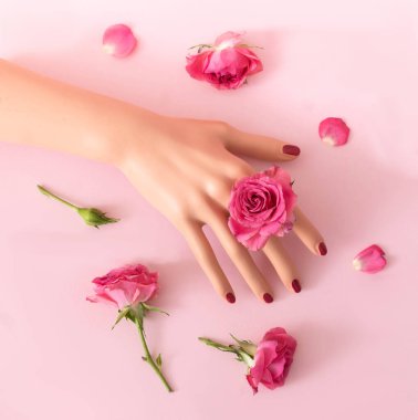 Yüzük olarak pembe gül, diğer güller ve pastel pembe arka plan olan bir kadın eli. Zarif moda lüks konsepti. Düz yatıyordu.
