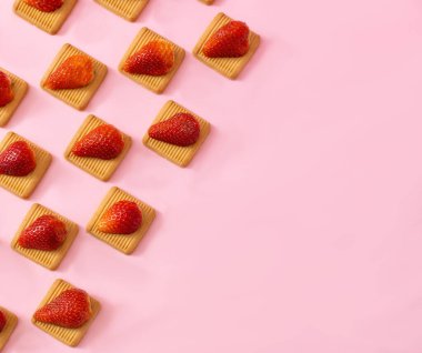 Taze çilekler bisküviler üzerinde dizilmiş pembe arka planda köşegen şeklinde fotokopi alanı ile. Minimum bahar yaz atıştırmalığı estetiği.