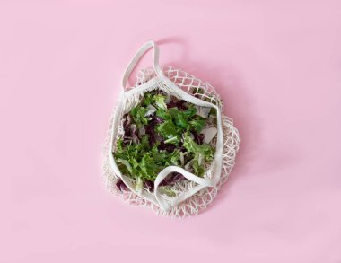 Pembe arka planda yeşil ve kırmızı salata yaprakları olan bir örgü çantası. Sağlıklı yaz vitaminleri konsepti. Çeşitli ticari kullanım için duvar kağıdı. Düz yatıyordu. Boşluğu kopyala.