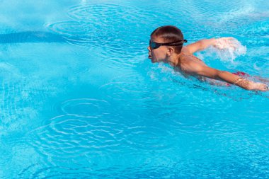 Yüzücü çocuk havuzda havuzda kelebek gibi yüzüyor. Genç sporcu yüzme havuzunda yüzüyor, yarışmadan önce antrenman yapıyor. Su sporları, sağlıklı yaşam tarzı, çocuk sporu.