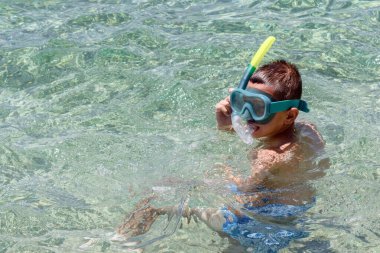 Şnorkeli ve maskesiyle berrak deniz suyunda yüzen çocuk plaj aile tatilinin tadını çıkarıyor. Dalış, yüzme, su sporları konsepti. Yaz tatili arka planı, kopyalama alanı