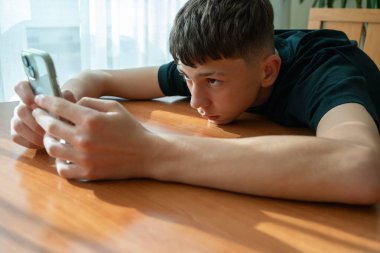 Genç çocuk oturuyor, akıllı telefon ekranına odaklanmış, daktilo ediyor, oynuyor ya da etkileşime geçiyor. Gen Z 'nin teknolojiye olan bağlantısı, modern dijital, oyun odaklı gençlik kültürü, ekran zamanı, hareketli davranış