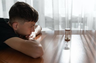 Genç bir çocuğun sembolik ve duygusal portresi. Doğal ışık ve yumuşak gölgelerle dolu küçük kum saatine dikkatle bakıyor. Dinginliği ve iç odağı yansıtıyor. Farkındalık, zaman kavramı