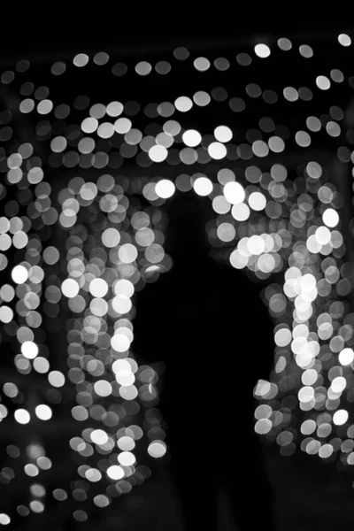 Black and white photo, abstract blur bokeh background with a silhouette of woman. Lonely person alone among the festive Christmas lights. Stress, depression, lost soul, problems, hopelessness