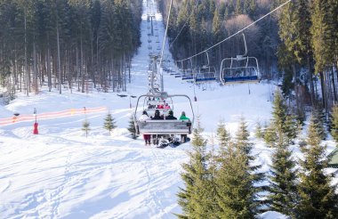 Sandalye kaldırma, tanınmayan kayakçıları Karpat dağlarının karla kaplı yamacına taşıyor. Soğuk kış güneşli bir gün, açık hava aktiviteleri. Kayak eğitimi. Kış sporları. Mevsimlik kış sevinçleri