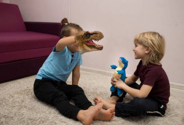 Anaokulu çocukları yerde oturmuş dinozor oyuncaklarıyla oyun oynuyorlar. Arkadaşlarla iletişim, kardeşler arasındaki arkadaşlık, neşeli bir çocukluk. Seçici odaklanma. çocuklar için eğlence.