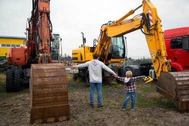 Adam ve çocuk, el ele tutuşup, sırtlarını dönerek, kazıcıların büyük kovalarla yer aldığı şantiyeye bakıyorlar. Oğlunun inşaat malzemelerine olan tutkusu. Oğlan için ilginç geziler.