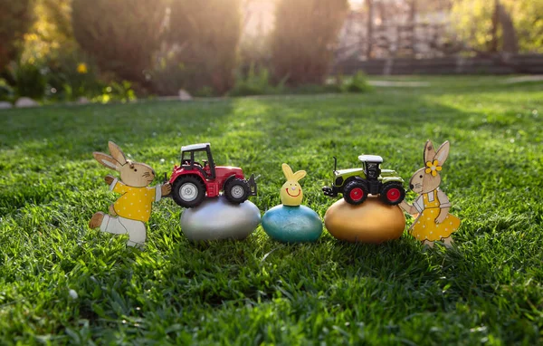 models of toy models of two tractors, brightly colored eggs and easter bunnies lie on the grass. Business concept for Easter greetings for farming and agriculture. easter card. copy space