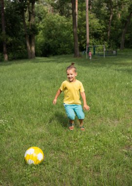 boy of 5-6 years old runs in the park on green grass and kicks a yellow soccer ball. Active lifestyle, fun activities for children in the summer outdoors