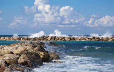 Dalgalar kayalık kıyıya çarpıyor. Güzel deniz manzarası. Köpüklü deniz ve su sıçramaları. Mavi turkuaz su ve güzel güneş ışığı bulutları