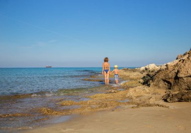 Güneşli bir günde, oğlu mayolu genç bir anne sırt sırta durarak mavi denize bakıyor. Hoş bir eğlence, yaz tatili. Anın zevki, mutlu annelik. Anneler Günü