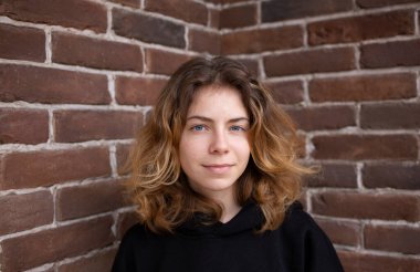 Portrait of a cute pretty young woman 18-19 years old, a girl - a teenager, a successful college student against a brick wall. Real people, everyday life