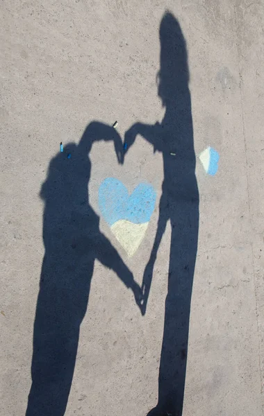 contrasting shadows of adult and child, hugging yellow-blue heart drawn with crayons on pavement . Ukrainians want peace. Childhood during the war. Love your homeland - Ukraine