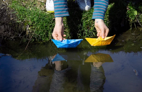 female hands launch paper boats of yellow and blue colors of the Ukrainian flag into the water. Symbol of freedom, independence. Drawing attention to the war in Ukraine. Patriotic children games