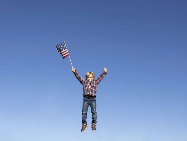 6岁的爱国男孩拿着美国国旗在蓝天上跳起来 快乐的飞吧积极的情绪 庆祝美利坚合众国独立日 — 图库照片