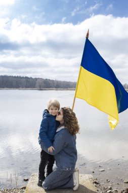 Oğlan ve genç kadın, Ukrayna bayrağıyla gölün yanındaki küçük kardeş ve yetişkin kız kardeş. Aile, birlik, mülteciler, destek. Ukrayna 'nın yanında dur. Rusya ile savaşı durdurun. mülteci ve göçmen sorunları