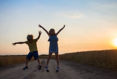 Neşeli kız ve oğlanların siluetleri gün batımının arka planında neşeyle zıplıyorlar. Eğlence, heyecan. çocukluk, yaz yürüyüşleri, arkadaşlık
