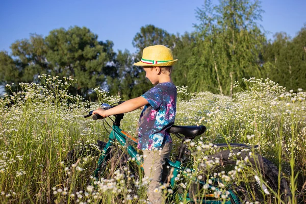 boy with a bicycle stands in a meadow with flowers. concept of a healthy active lifestyle in nature. cycling, travel, summer holidays outside the city