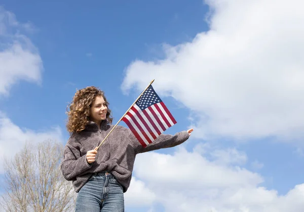 在阳光灿烂的日子 18岁的成年美丽而快乐的女孩手牵着美国国旗 与蓝天相映成趣 7月4日庆祝 美利坚合众国独立日 — 图库照片